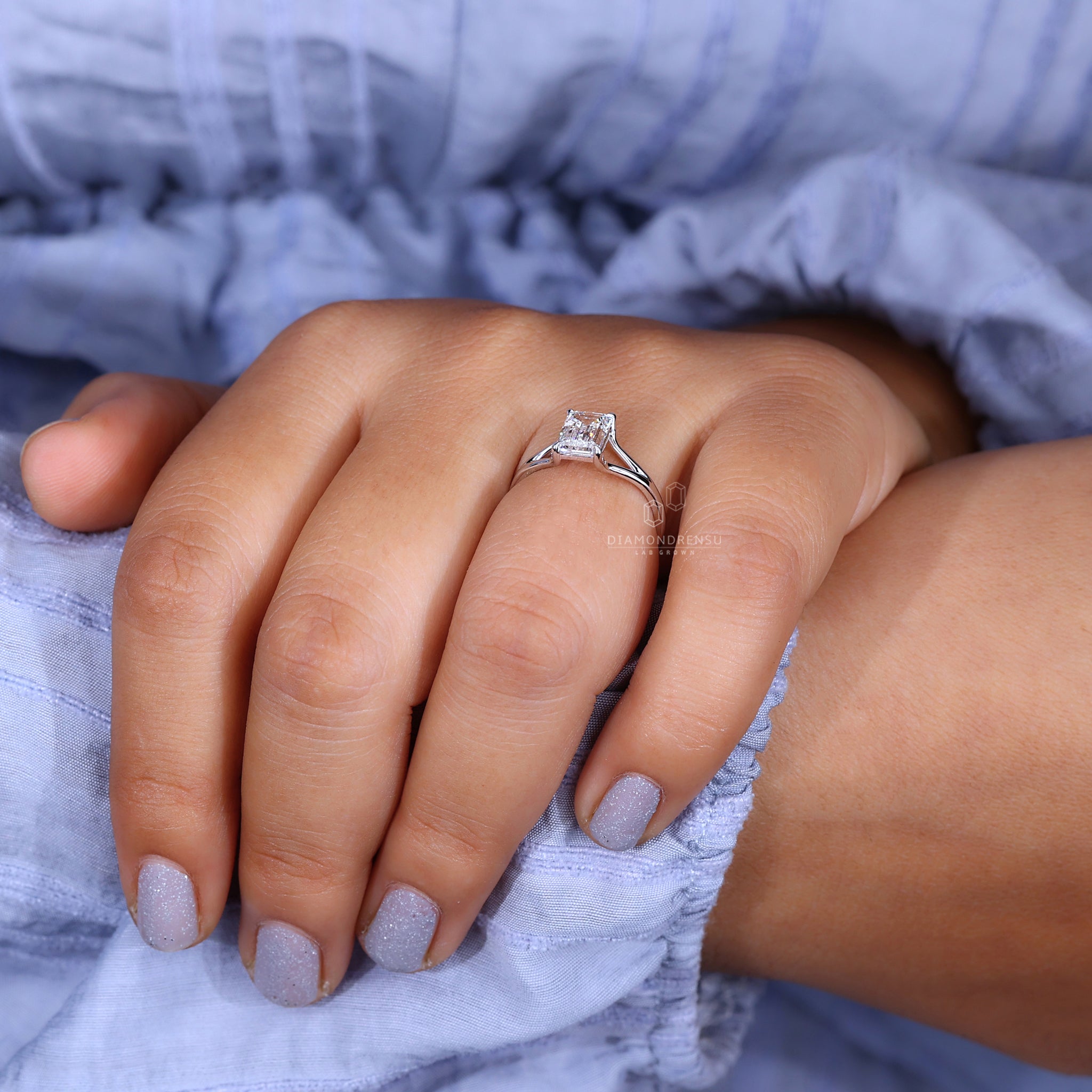 Model showing off a solitaire emerald cut ring in a white gold setting.