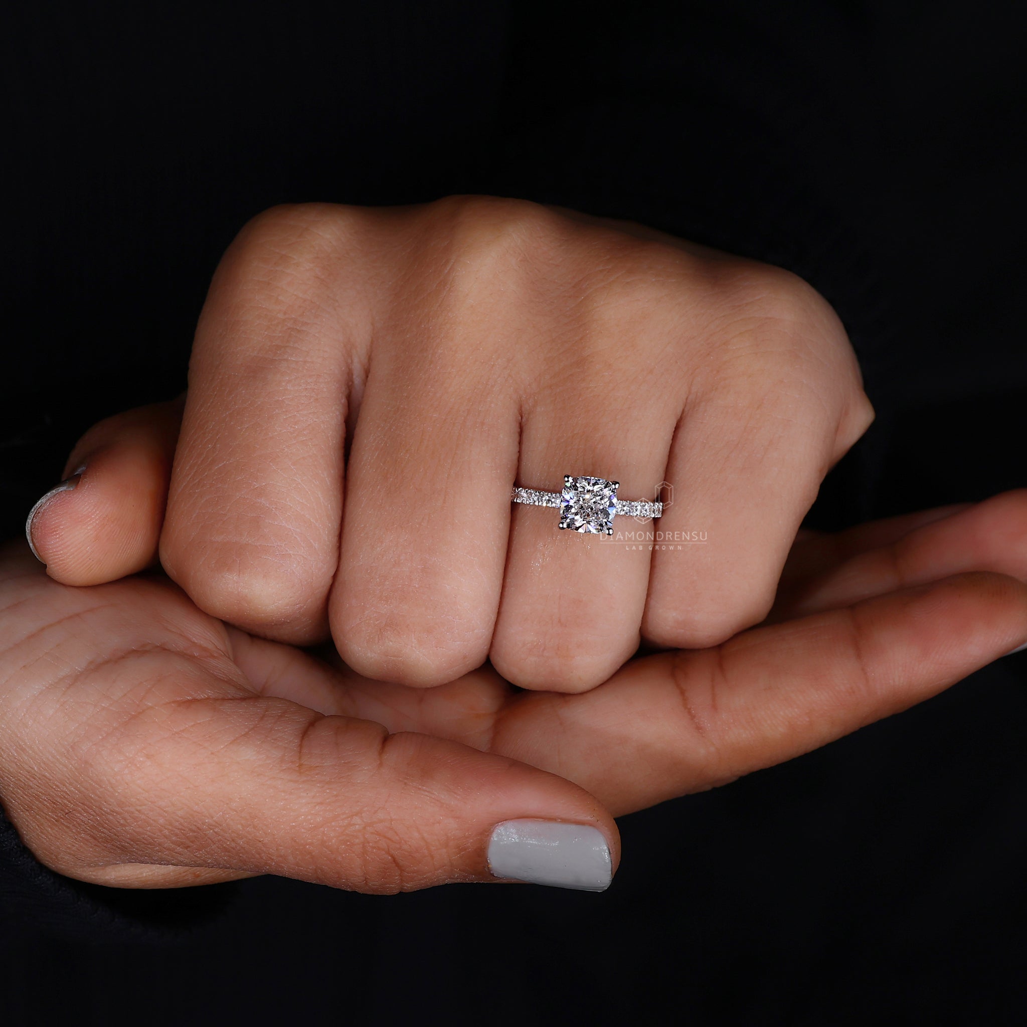 Elegant cushion cut ring with pave diamond setting on a model's finger.