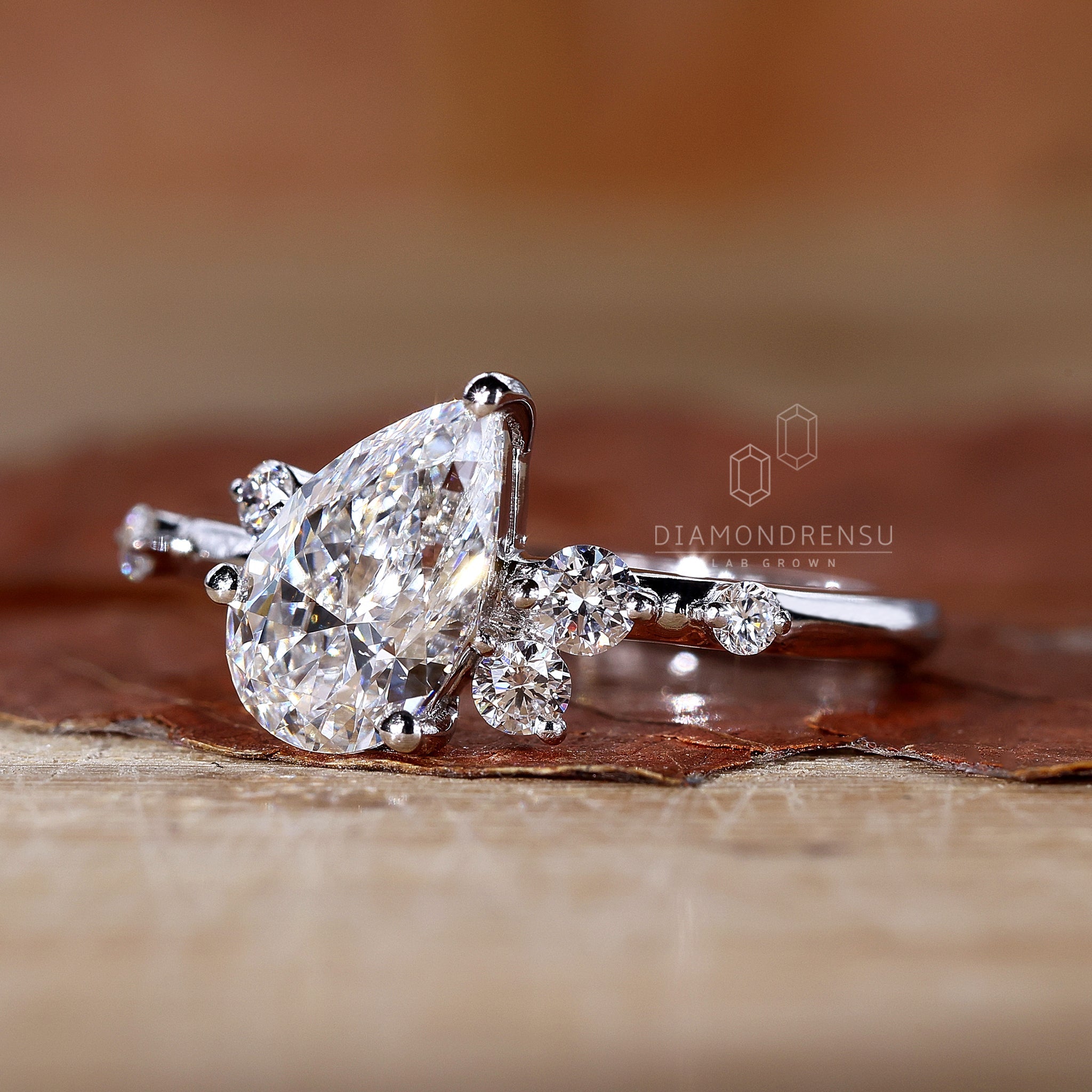 Diamondrensu engagement ring showcasing a pear-shaped diamond and round side stones.